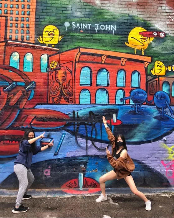 Amy and a friend posing in front of a colourful mural